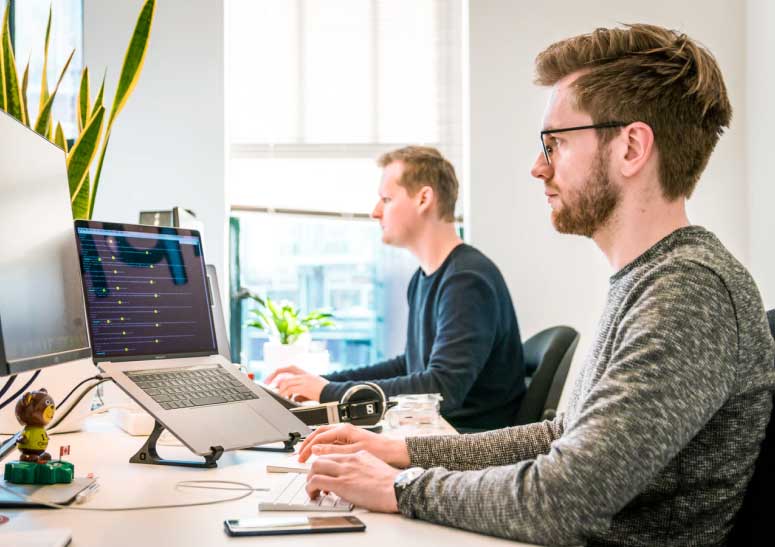 two men sitting at a desk working on a computer offering customer support services.